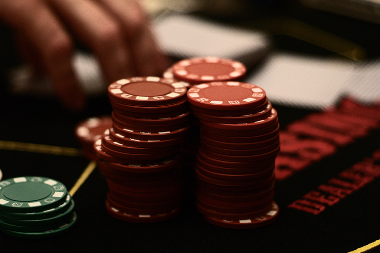 Close-up view of stacked red poker chips on a dark gaming table, showing their white striped edges and smooth surfaces